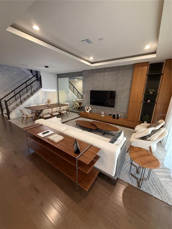 A modern living room features a large sectional sofa, wood shelving, and a wall-mounted television — 8289 TOPSAIL PLACE, WINTER GARDEN, FL