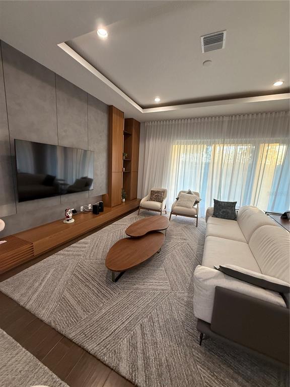 A modern living room features a large television, wood cabinetry, and a tiered coffee table — 8289 TOPSAIL PLACE, WINTER GARDEN, FL