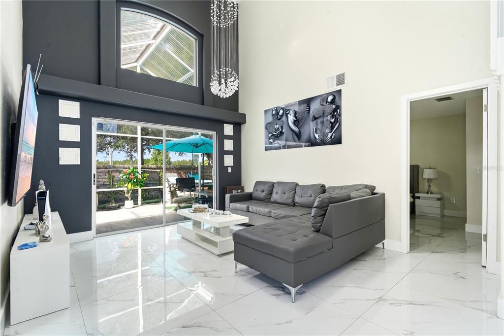 A modern living room features a grey sectional sofa, white tile floors, and high ceilings — 2724 EMERSON LANE, KISSIMMEE, FL