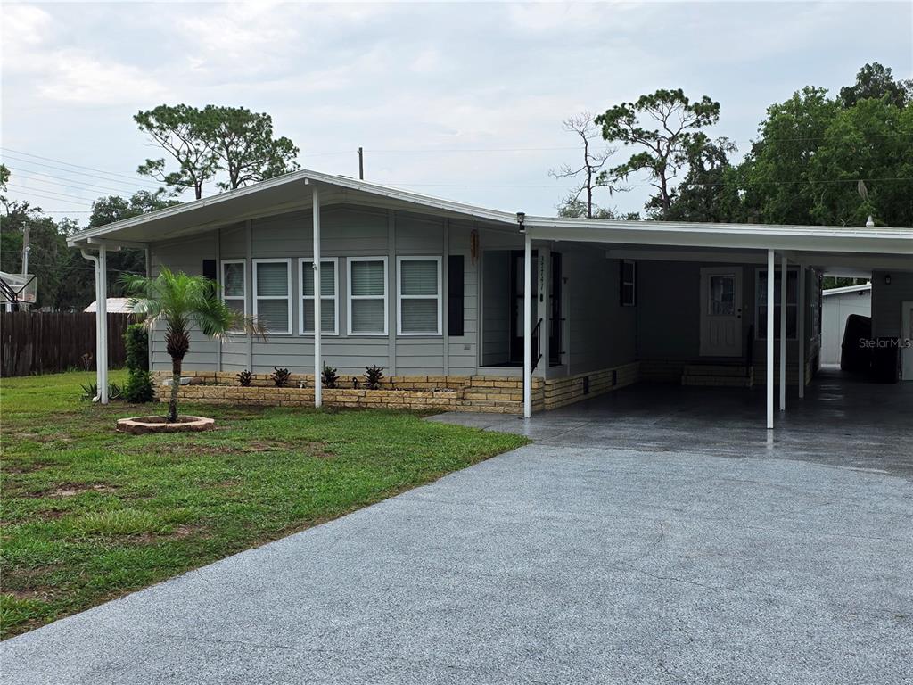 A gray manufactured home features a front porch, a carport, and a brick foundation — 37747 SILVER PINES AVENUE, ZEPHYRHILLS, FL
