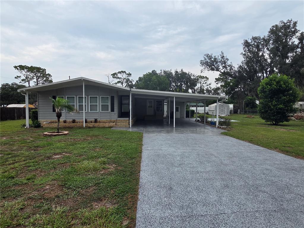 A single-story house with gray siding, a large carport, and a paved driveway — 37747 SILVER PINES AVENUE, ZEPHYRHILLS, FL
