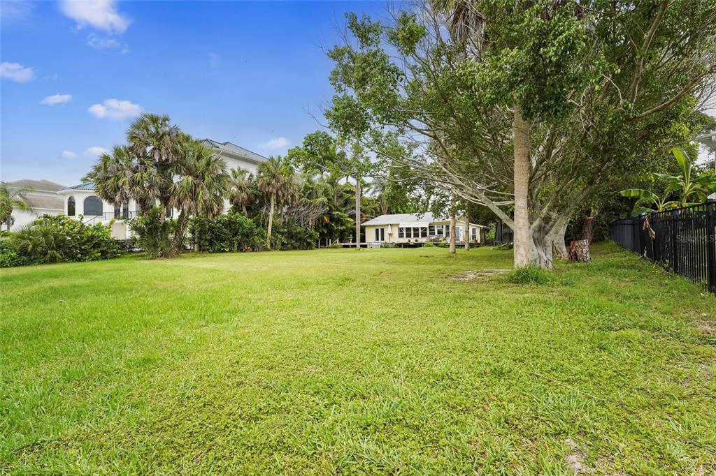 A large, grassy backyard features mature trees, lush landscaping, and a distant single-story house — 7538 WESTMORELAND DRIVE, SARASOTA, FL