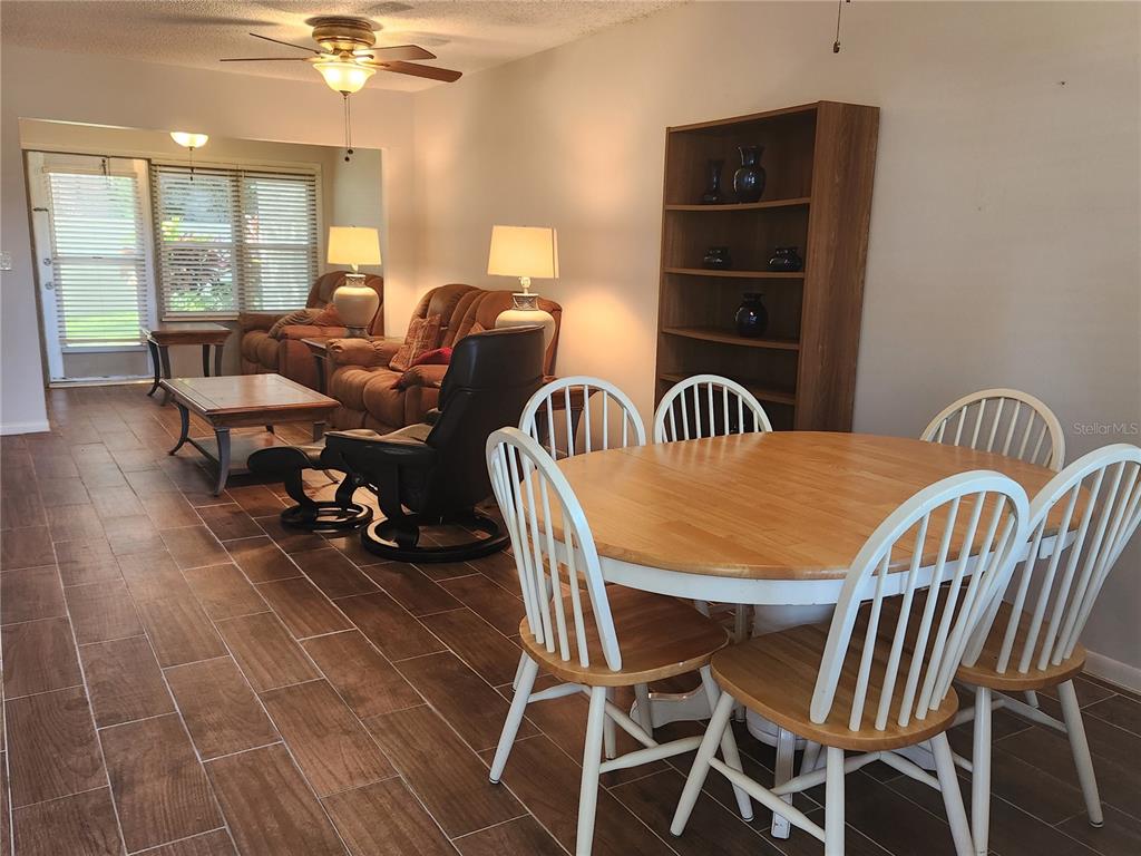 A dining area with a wooden table and chairs sits in front of a living room — 1701 PINEHURST ROAD UNIT 34D, DUNEDIN, FL