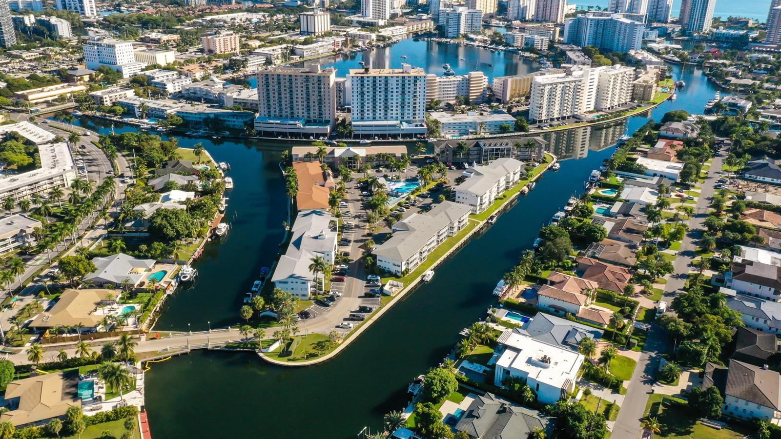 An aerial view shows residential buildings, canals, and swimming pools in a coastal neighborhood — 450 Paradise Isle Boulevard, Hallandale Beach FL 33009, HALLANDALE BEACH, FL