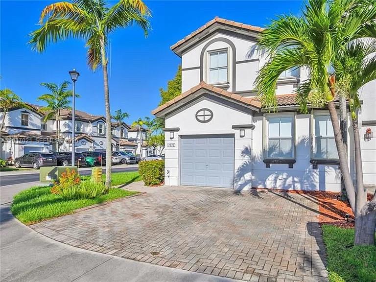 A two-story house with a paved driveway and palm trees sits under a clear sky — 7772 NW 114th Pl # 0, Doral FL 33178, DORAL, FL