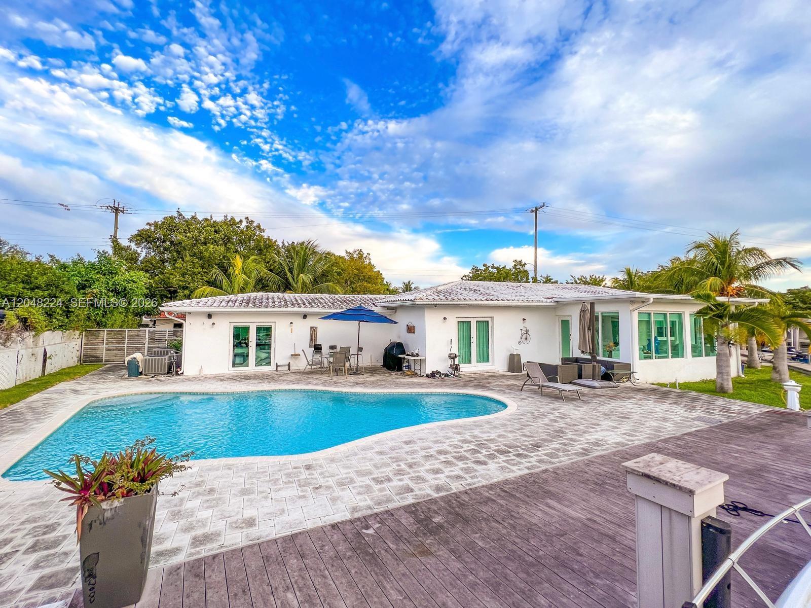A white house with a tiled roof features a swimming pool and a wooden deck — NORTH MIAMI, FL