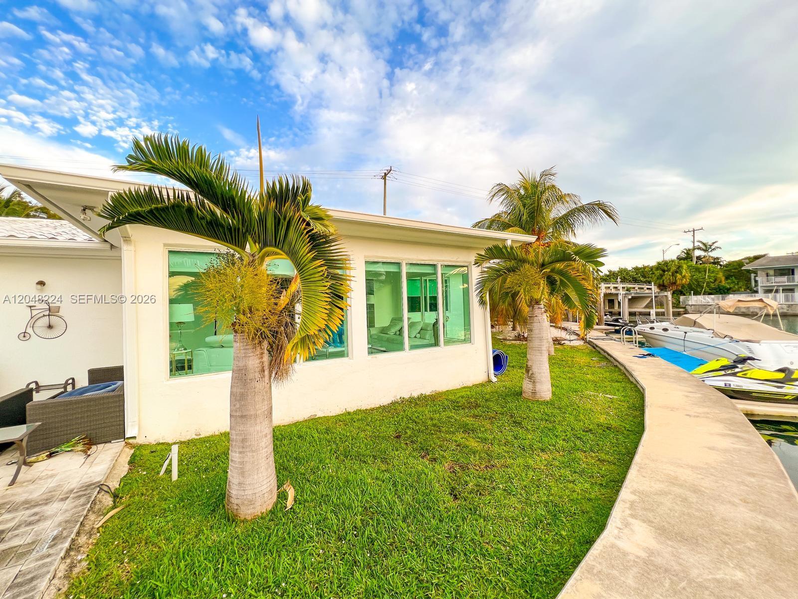 A white house exterior features two palm trees, large windows, and a waterfront dock — NORTH MIAMI, FL