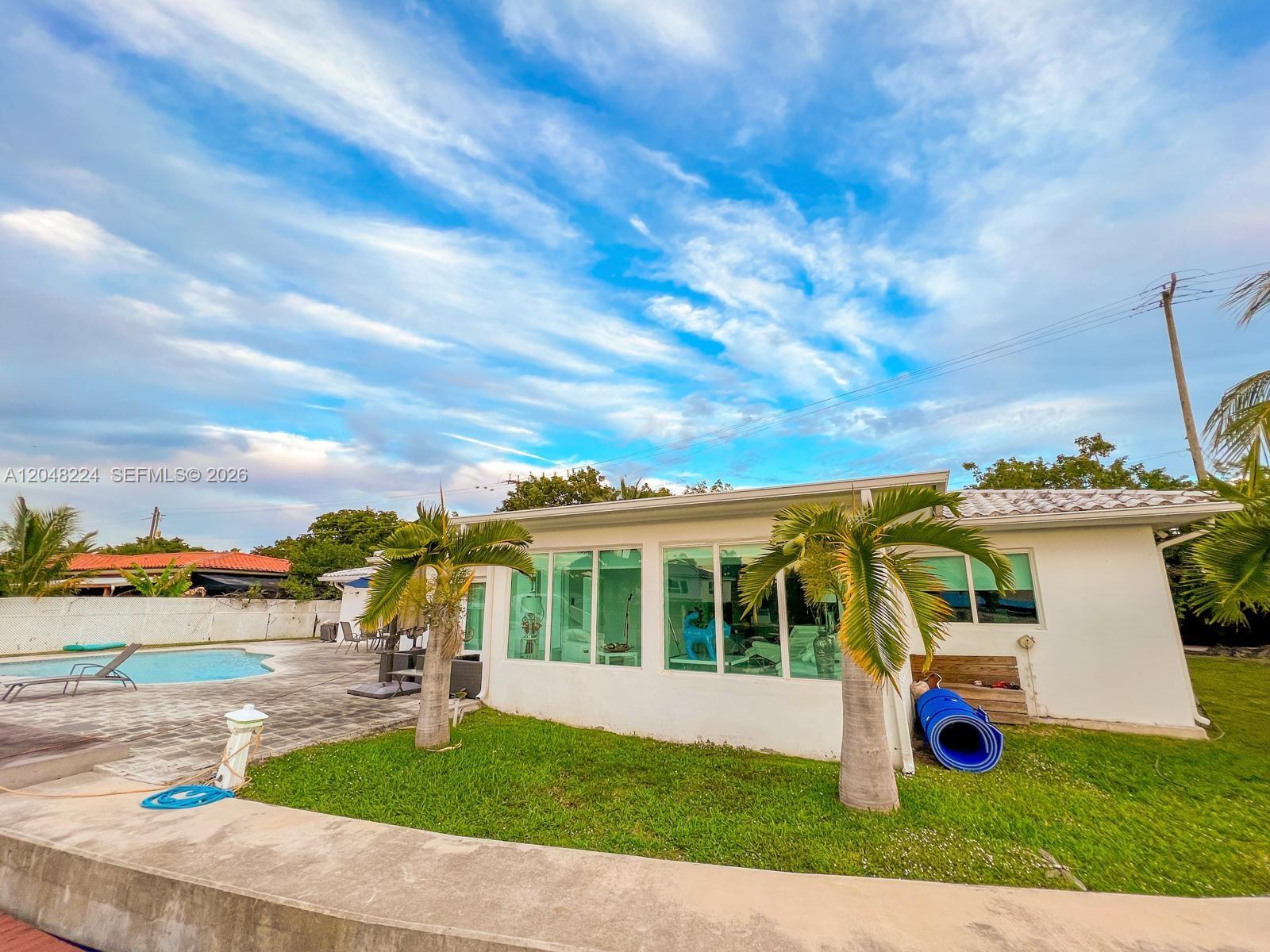 A white house with large windows sits beside a swimming pool and two palm trees — NORTH MIAMI, FL
