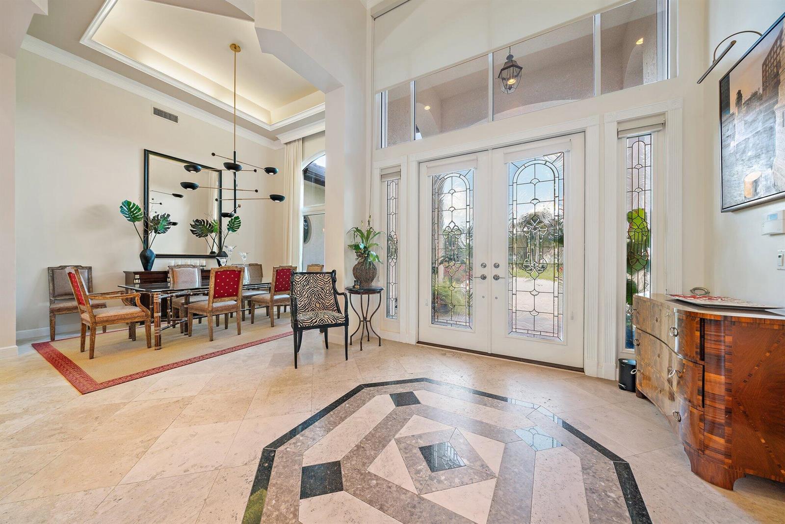 A bright foyer with stone flooring leads into a dining room featuring a modern chandelier — 8010 Fairway Lane, West Palm Beach FL 33412, WEST PALM BEACH, FL