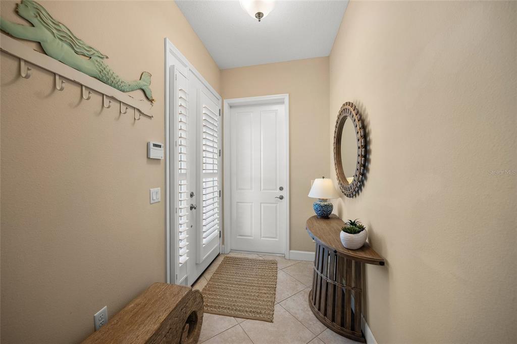 An entryway features a tiled floor, a wooden console table, a mirror, and a mermaid-themed rack — 229 SAPPHIRE LAKE DRIVE UNIT 201, BRADENTON, FL