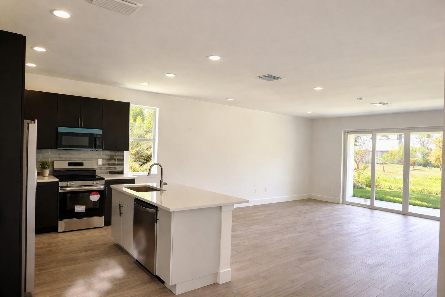A modern kitchen with dark cabinets and a white island opens to a spacious living area — 500 Sunset Road N, FL 33947, FL