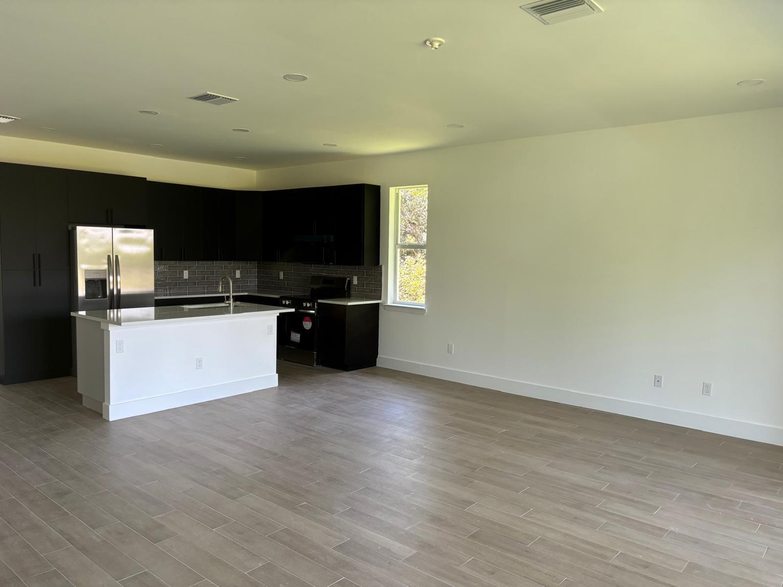A modern kitchen with dark cabinetry, a white island, and light wood-look tile flooring — 500 Sunset Road N, FL 33947, FL