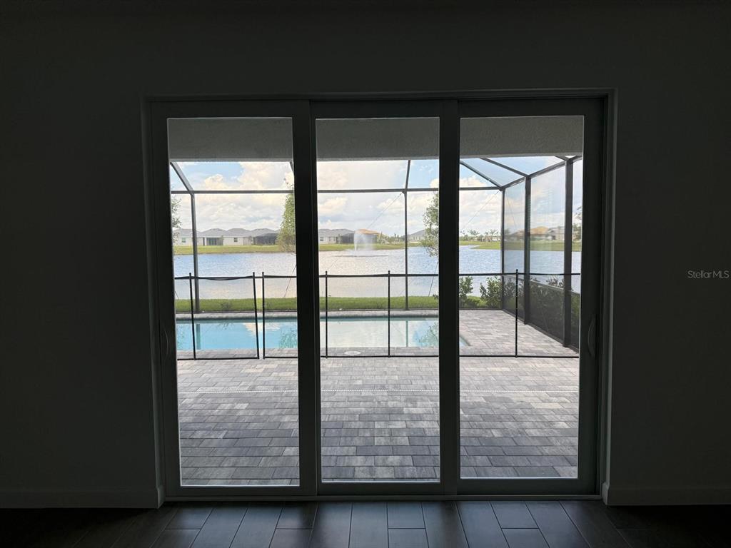 A view through sliding glass doors shows a pool, patio, and lake with a fountain — 7913 LAKES EDGE LANE, PORT CHARLOTTE, FL