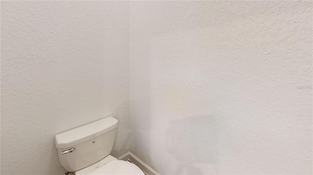 A white toilet is positioned in the corner of a room with white textured walls — 7913 LAKES EDGE LANE, PORT CHARLOTTE, FL