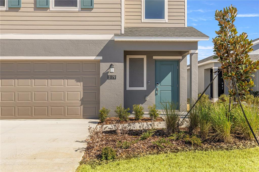A two-story house exterior features a tan garage, a teal front door, and landscaping — 8107 SW 45TH COURT, OCALA, FL