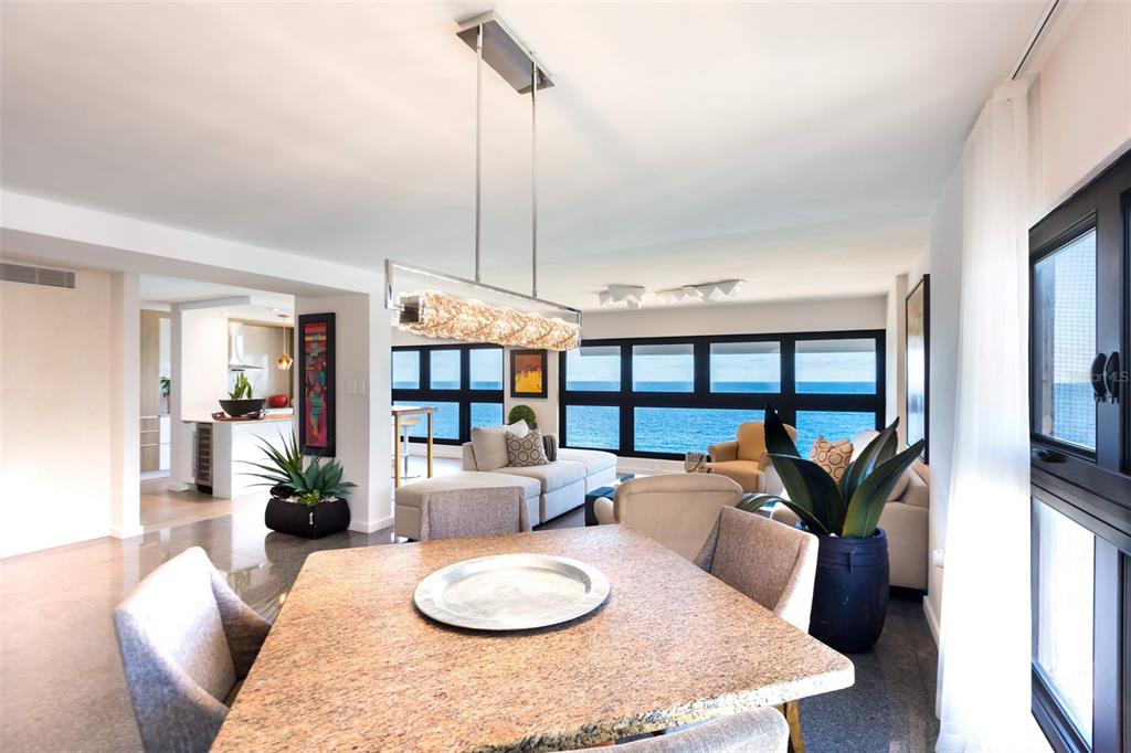 A dining area with a stone table overlooks a living room and ocean view windows — 1507 ASHFORD AVE. AVENUE UNIT 1201, SAN JUAN, PR