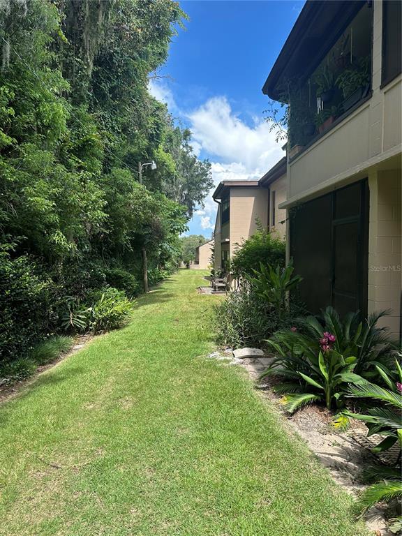 A grassy path runs between a multi-story apartment building and a dense line of trees — 2415 NE 7TH STREET UNIT 2, OCALA, FL