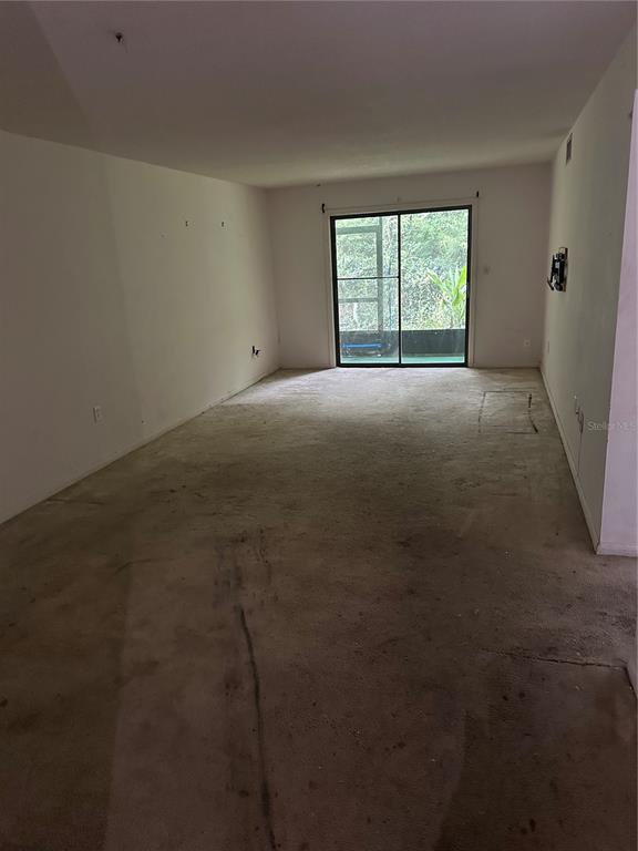 An empty living room with beige carpeting and a sliding glass door leading to a balcony — 2415 NE 7TH STREET UNIT 2, OCALA, FL