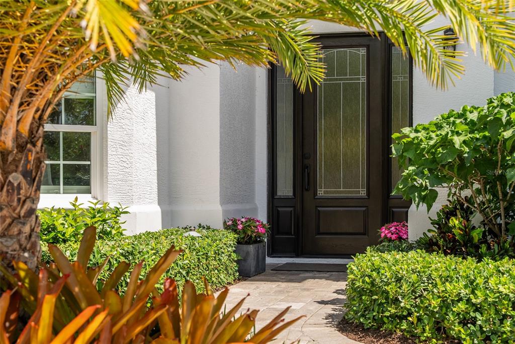 A dark wood front door with glass panels is surrounded by lush landscaping and palm trees — 1915 CLEMATIS STREET, SARASOTA, FL