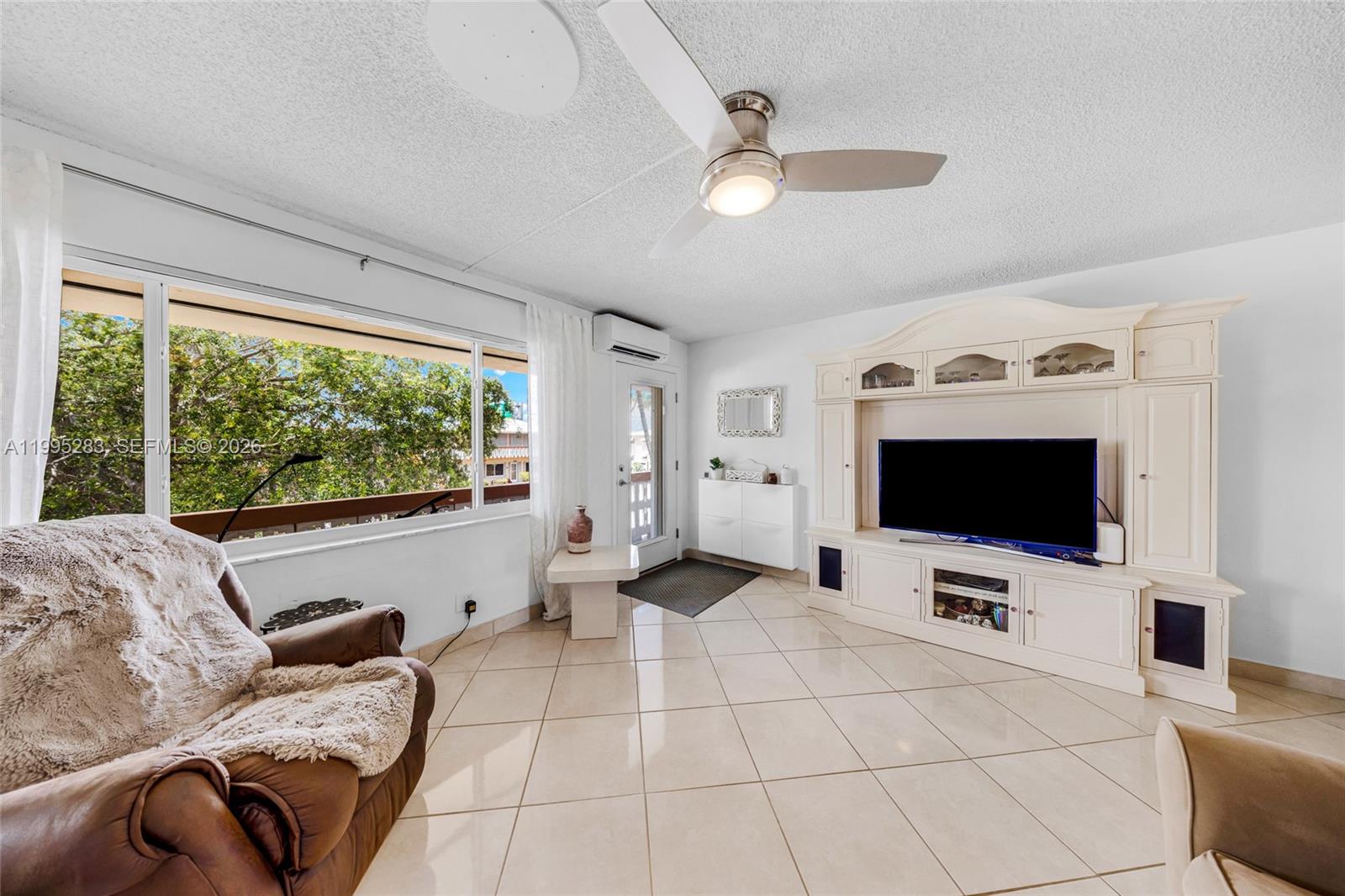 A living room features tile floors, a ceiling fan, a large entertainment center, and windows — 1015 SW 11th Ave # 15K, Hallandale Beach FL 33009, HALLANDALE BEACH, FL