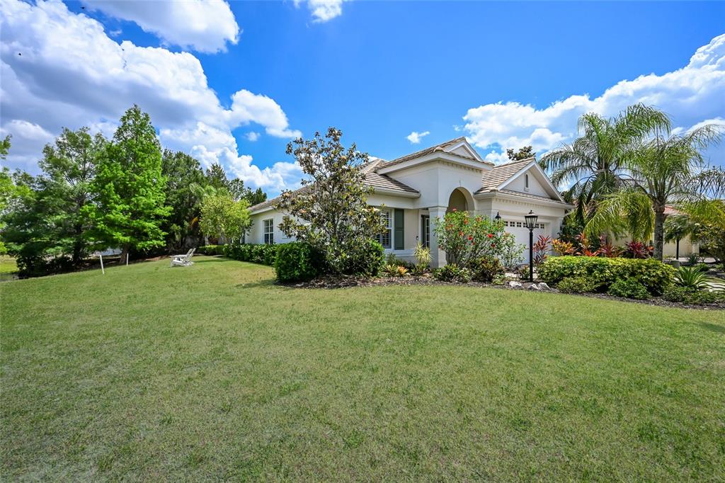 A single-story house with a tiled roof, a paved driveway, and a lake in the background — 15422 HELMSDALE PLACE, LAKEWOOD RANCH, FL