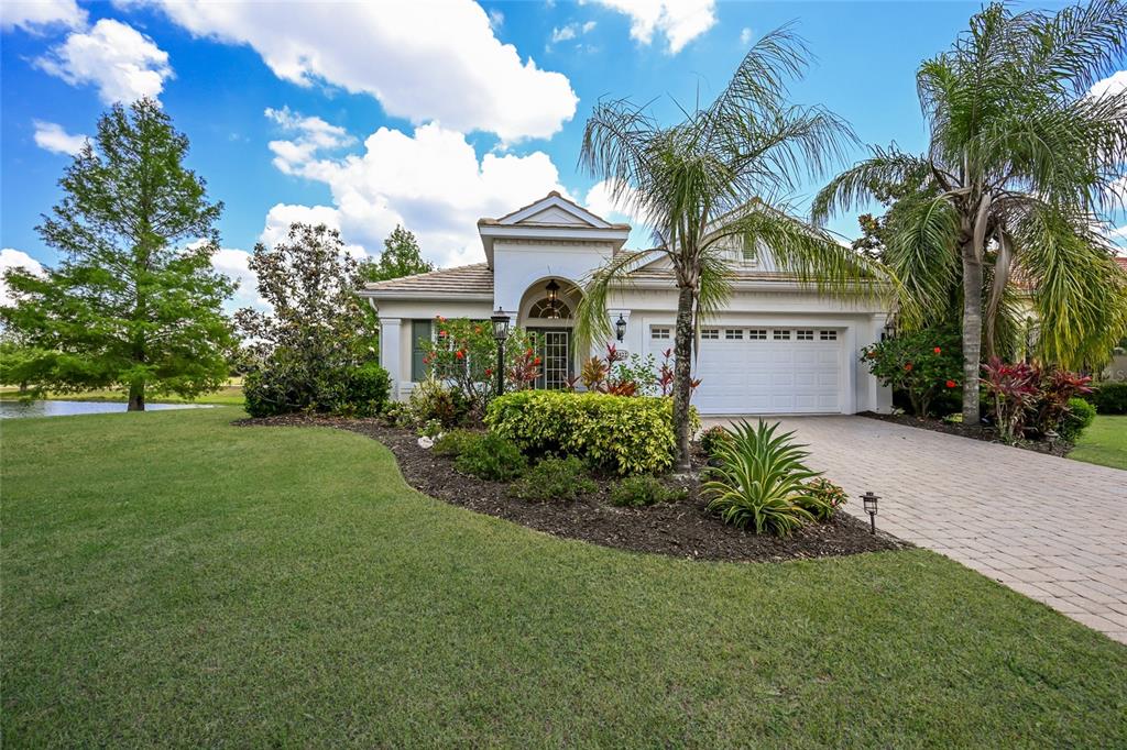 A single-story house with a beige stucco exterior, a tiled roof, and a large front lawn — 15422 HELMSDALE PLACE, LAKEWOOD RANCH, FL