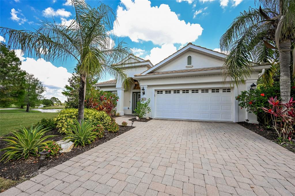A single-story house with a white garage, paved driveway, and palm trees under a blue sky — 15422 HELMSDALE PLACE, LAKEWOOD RANCH, FL