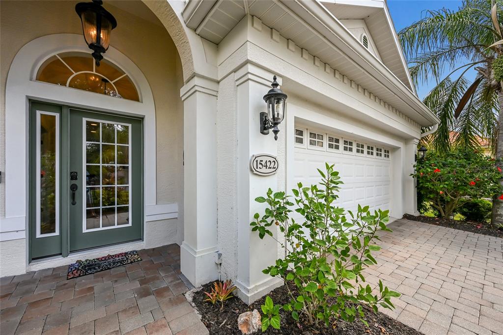 The exterior of a house features a green front door, a garage, and landscaping — 15422 HELMSDALE PLACE, LAKEWOOD RANCH, FL
