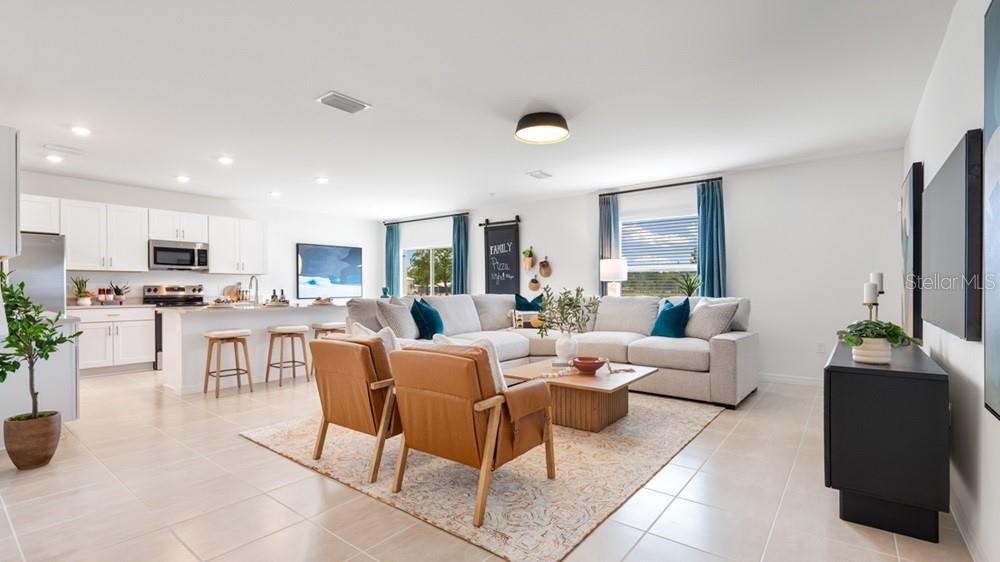 An open-concept living room and kitchen featuring white cabinetry, a sectional sofa, and leather chairs — 6523 EQUINOX LANE, NORTH FORT MYERS, FL