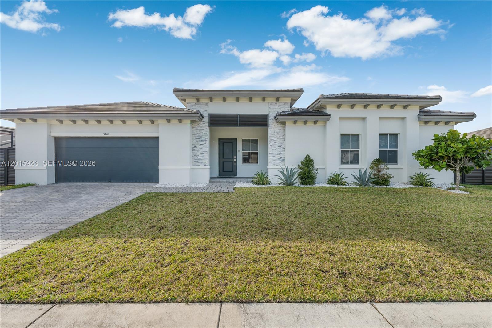 A modern single-story house features a gray garage, stone accents, and a landscaped front yard — 19100 SW 132nd Pl, Miami FL 33177, MIAMI, FL