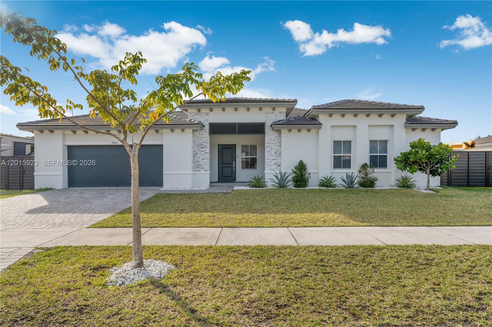 A single-story house with a white stucco facade, stone accents, and a dark garage door — 19100 SW 132nd Pl, Miami FL 33177, MIAMI, FL