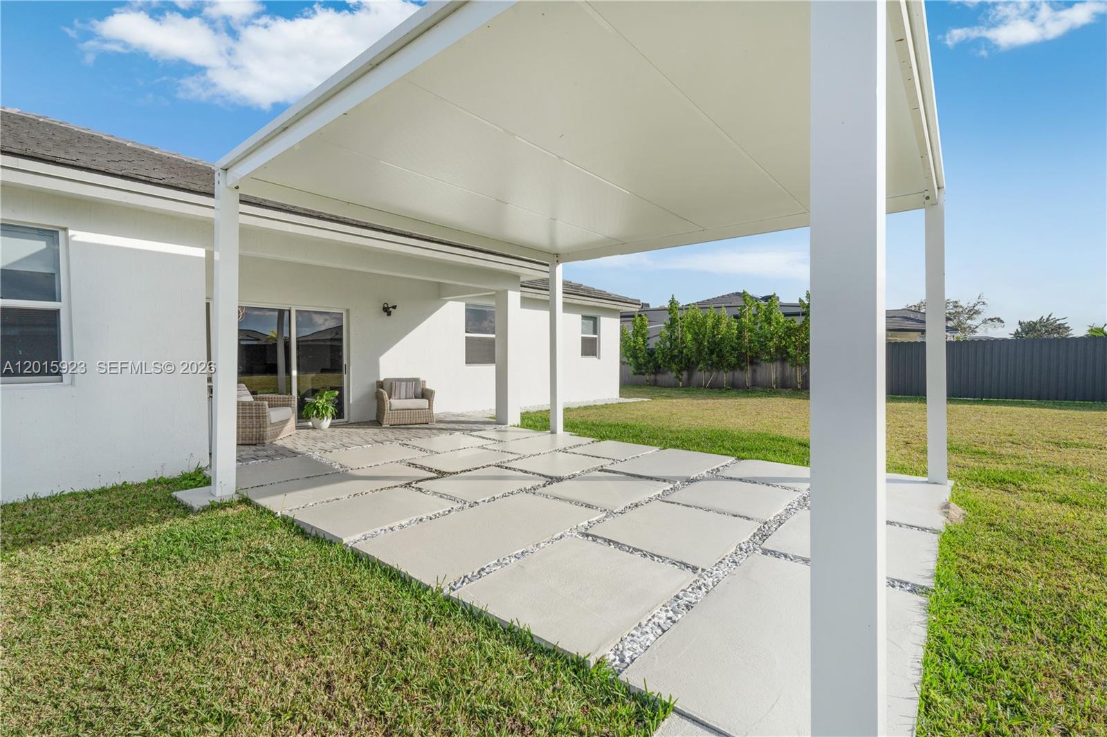 A white house features a covered patio with concrete pavers and gravel in the backyard — 19100 SW 132nd Pl, Miami FL 33177, MIAMI, FL
