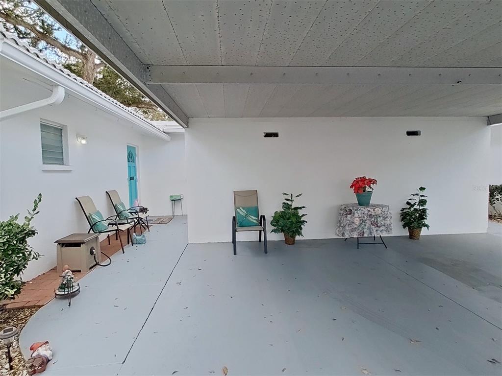 A covered carport with a gray concrete floor, white walls, and several chairs and plants — 1845 VERA PLACE UNIT 29, SARASOTA, FL