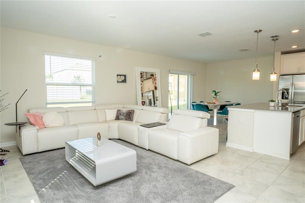A bright open-concept living room features a white sectional sofa, coffee table, and kitchen area — 2831 ALDER BERRY BOULEVARD, OCOEE, FL