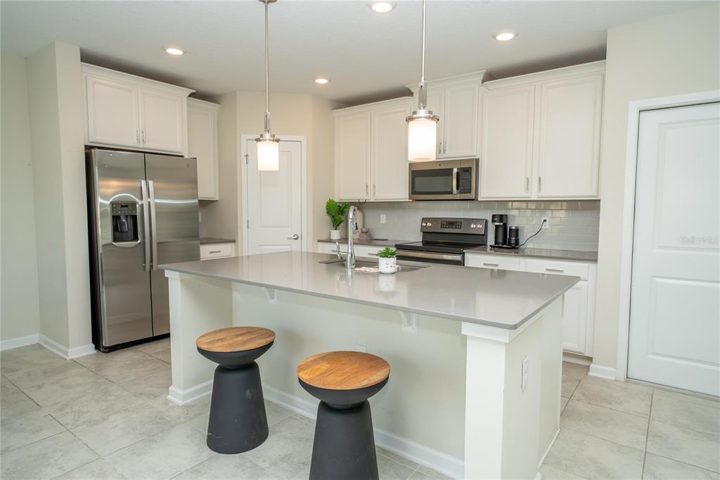 A kitchen with white cabinets, stainless steel appliances, a gray island, and two bar stools — 2831 ALDER BERRY BOULEVARD, OCOEE, FL
