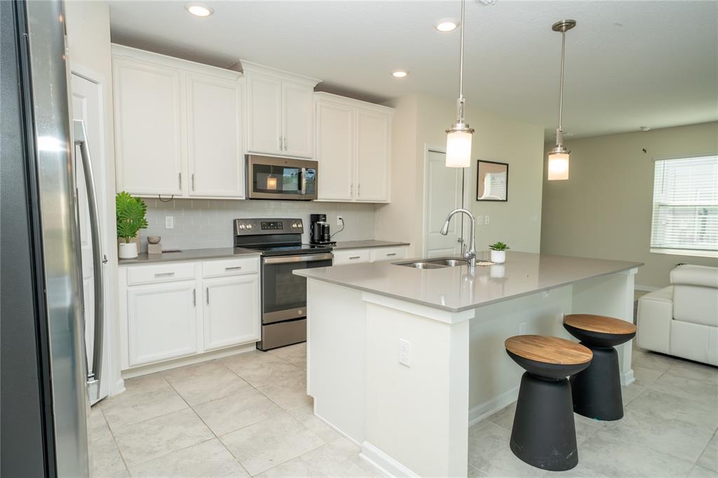 A modern kitchen features white cabinets, gray countertops, a central island, and two bar stools — 2831 ALDER BERRY BOULEVARD, OCOEE, FL