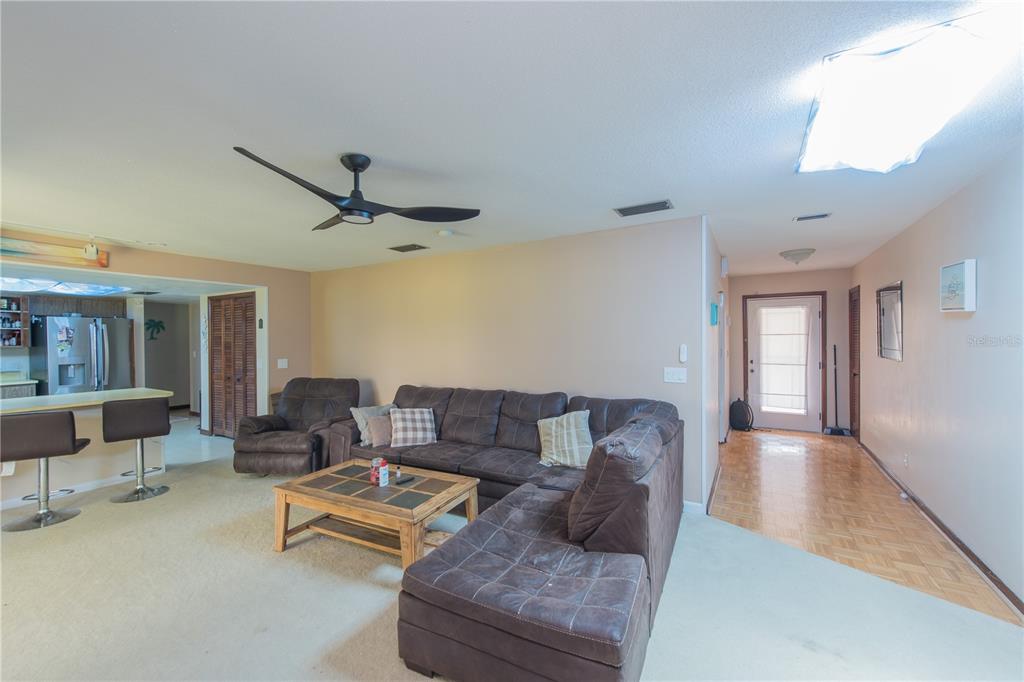 A living room with beige carpet and a ceiling fan opens to a kitchen with bar seating — 34 OAKMONT CIRCLE, ORMOND BEACH, FL