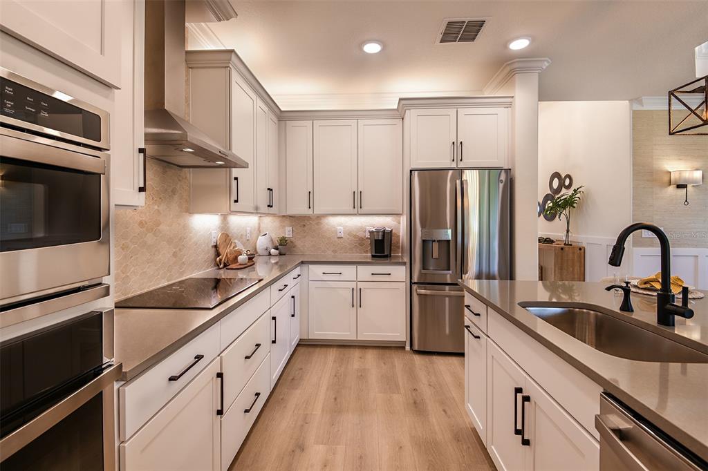 A modern kitchen features white cabinets, stainless steel appliances, and a large island with a sink — 11335 STRIPED BASS COURT, NEW PORT RICHEY, FL