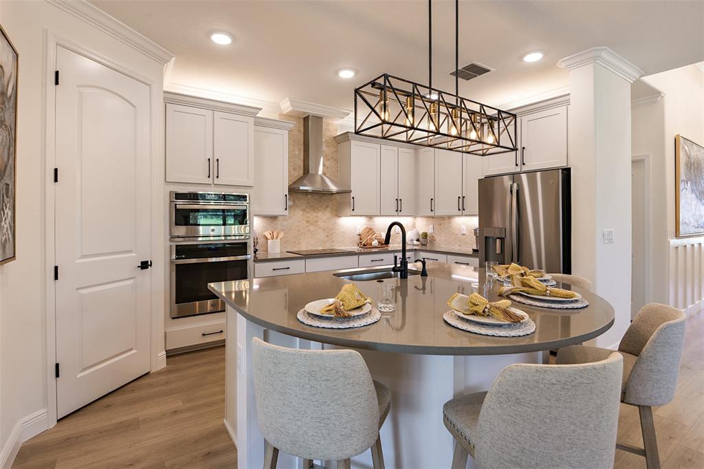A modern kitchen features white cabinetry, a curved island with bar stools, and stainless appliances — 11335 STRIPED BASS COURT, NEW PORT RICHEY, FL