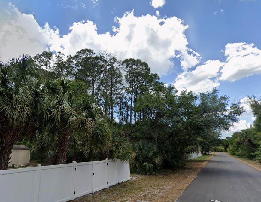 A white vinyl fence borders a wooded lot next to a paved residential street — 335 ORLEANS STREET, PORT CHARLOTTE, FL