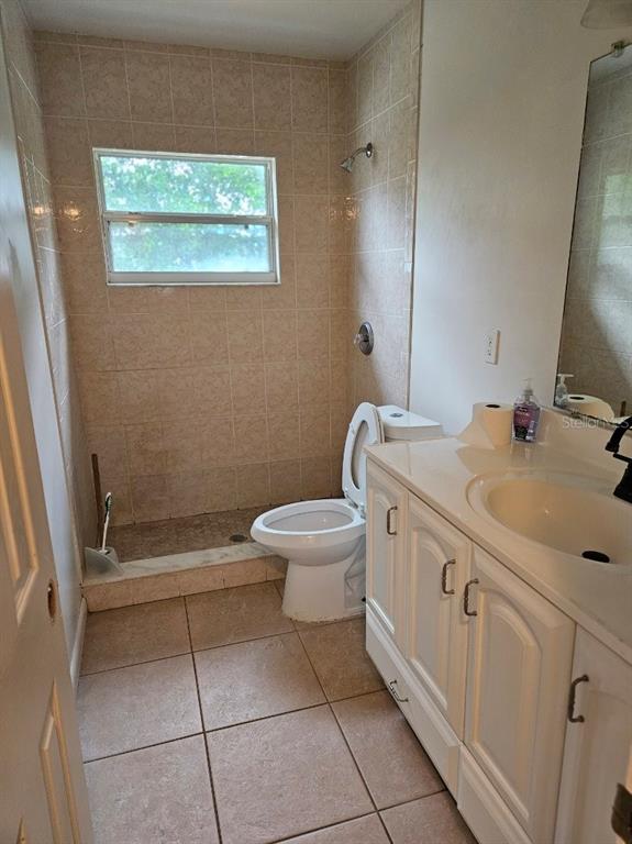 A bathroom features a tiled walk-in shower, a white toilet, and a vanity with sink — 1528 N POWERS DRIVE, ORLANDO, FL