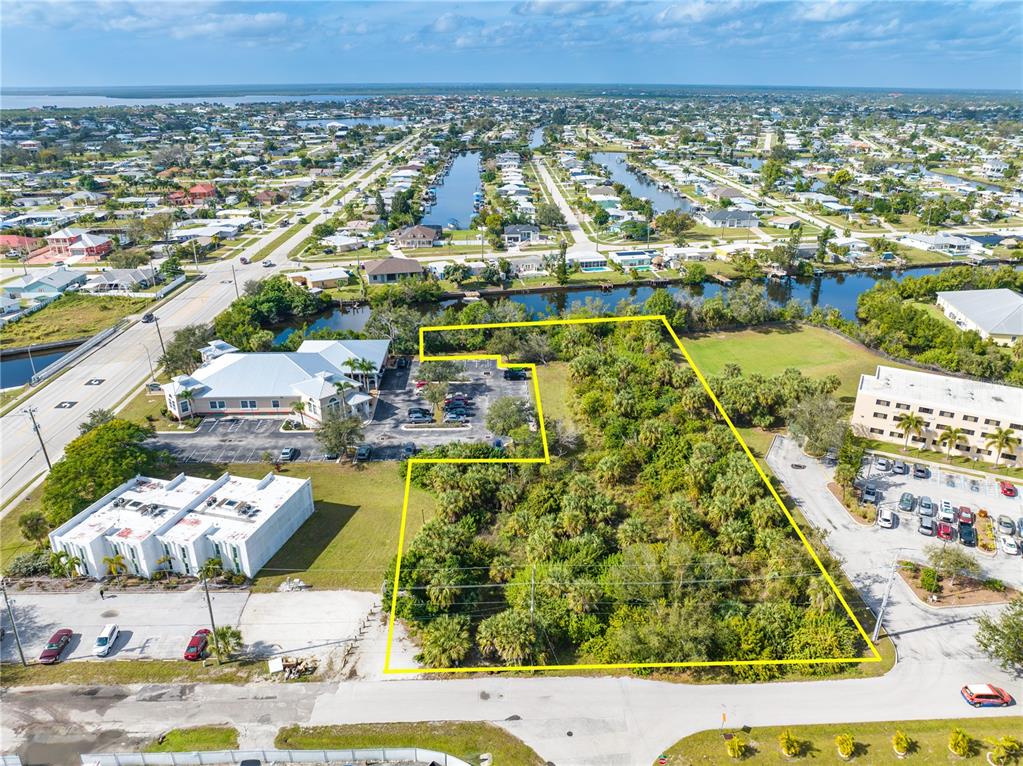 An aerial view shows a vacant, wooded lot outlined in yellow near commercial buildings — 4445 LISTER STREET, PORT CHARLOTTE, FL