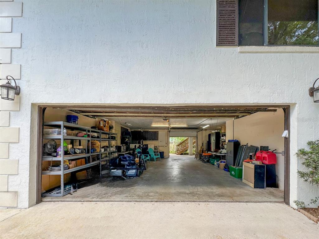 A wide, open-concept garage with concrete floors, metal shelving, and a rear exit to stairs — 40 CONCORD DRIVE, ORMOND BEACH, FL