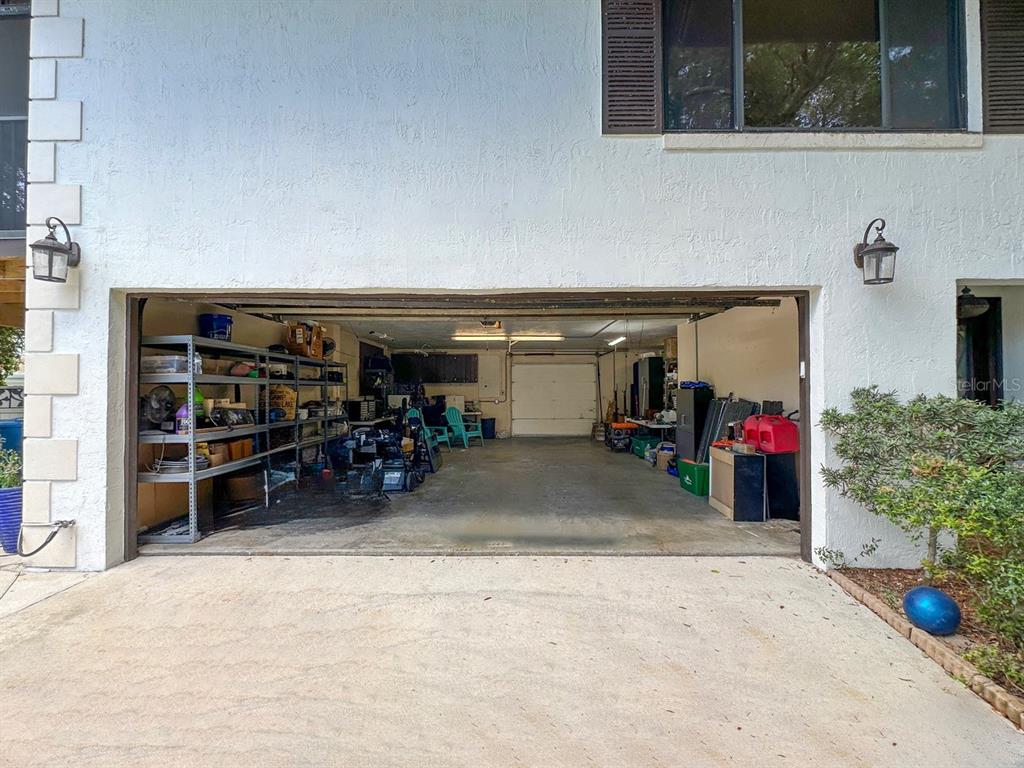 A wide, open garage with concrete flooring, storage shelving, and a rear roll-up door — 40 CONCORD DRIVE, ORMOND BEACH, FL