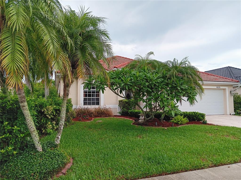 A single-story house with a red tile roof, a white garage, and a landscaped front yard — 6828 WINSLOW STREET, SARASOTA, FL