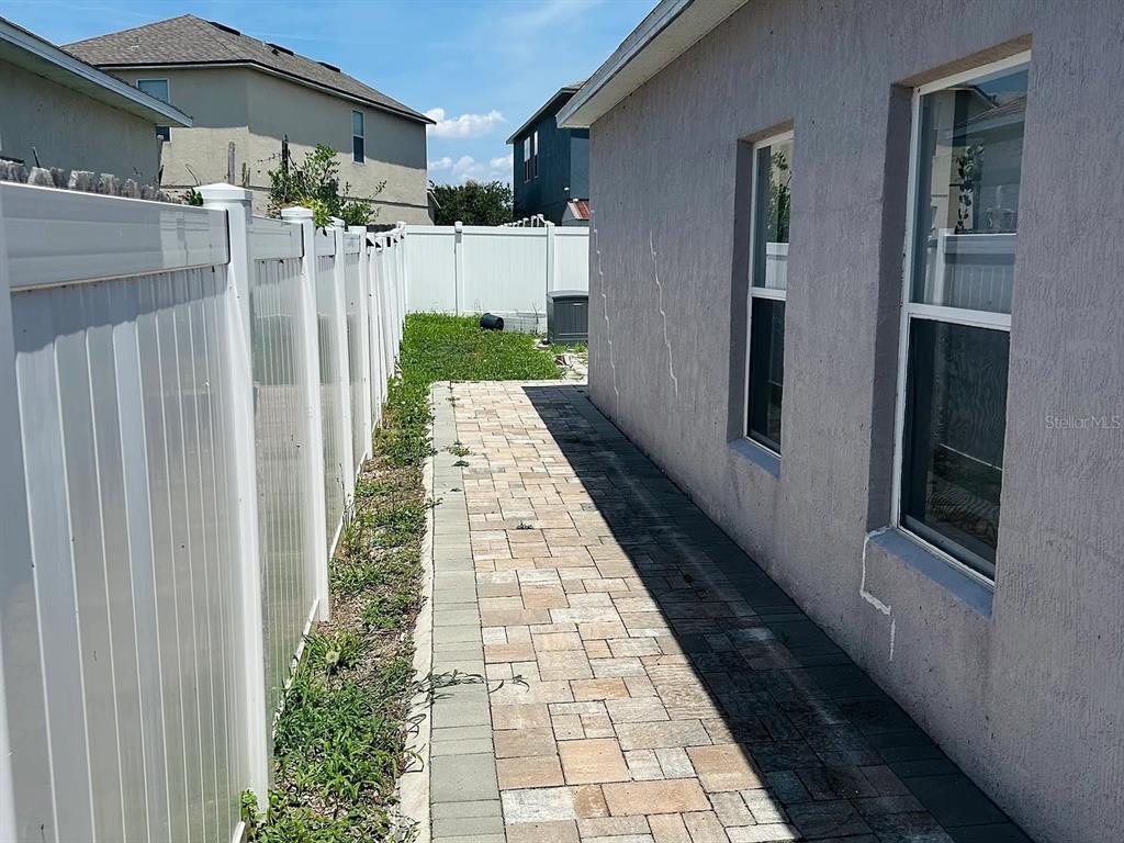 A paved walkway runs between a white vinyl fence and the side of a house — 7780 NEWLAN DRIVE, ORLANDO, FL