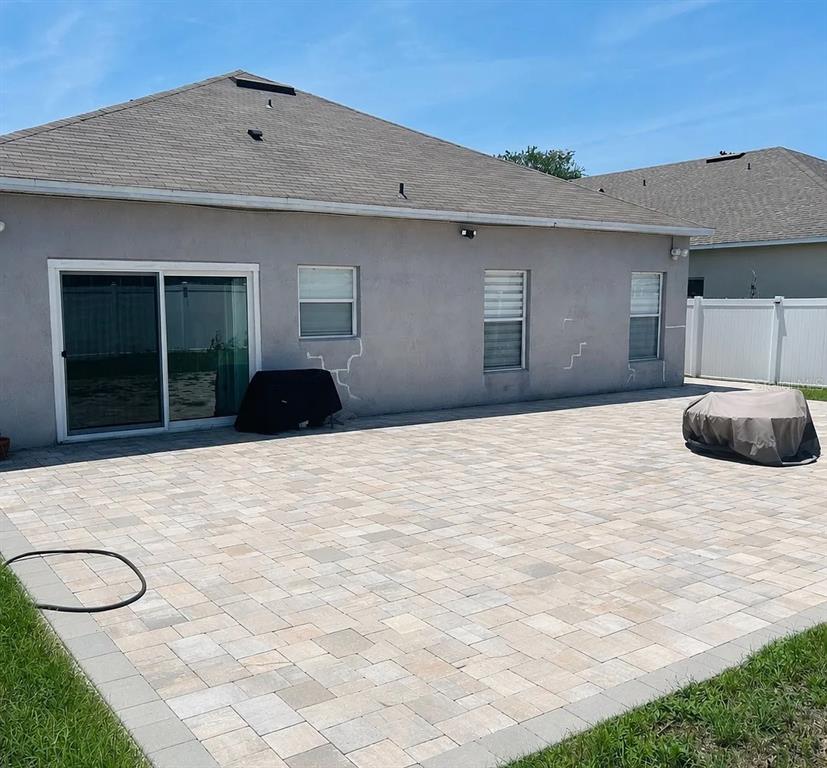 The exterior of a house features a large paver patio and visible cracks on the stucco — 7780 NEWLAN DRIVE, ORLANDO, FL