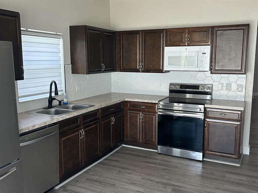A kitchen features dark wood cabinets, stainless steel appliances, and a white hexagonal tile backsplash — 7780 NEWLAN DRIVE, ORLANDO, FL