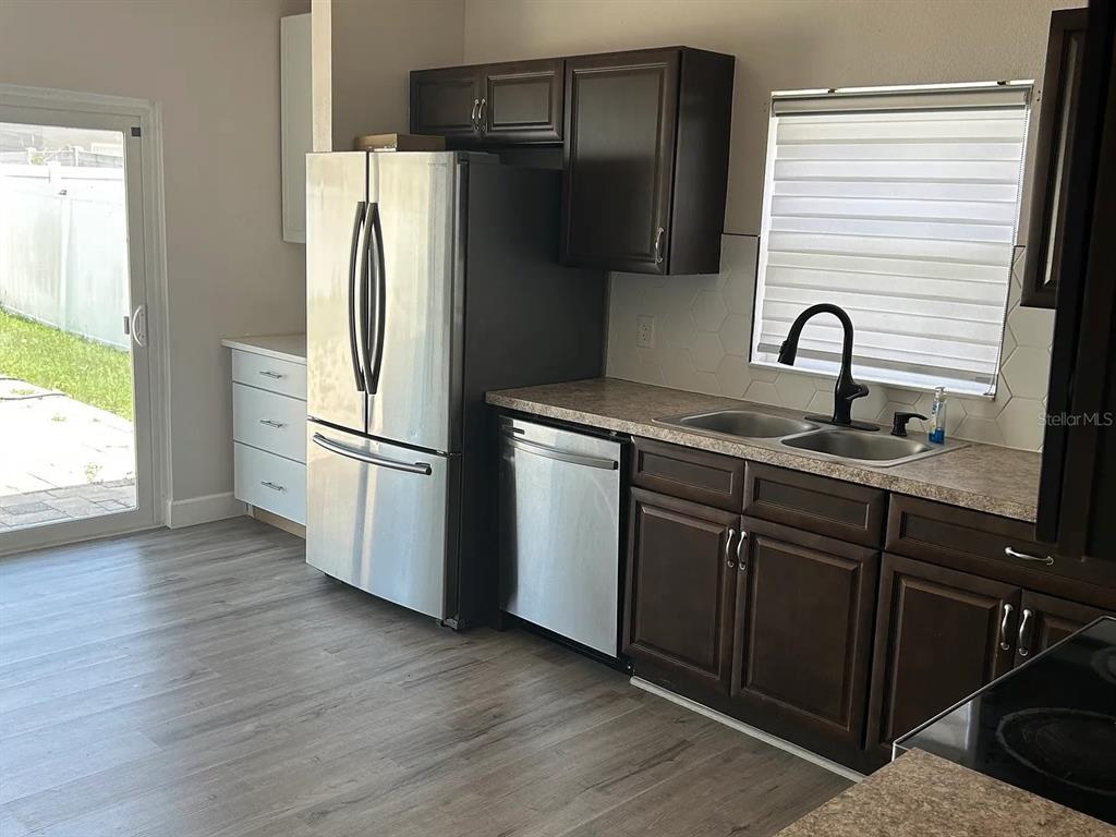 A kitchen features dark wood cabinets, stainless steel appliances, a double sink, and light flooring — 7780 NEWLAN DRIVE, ORLANDO, FL
