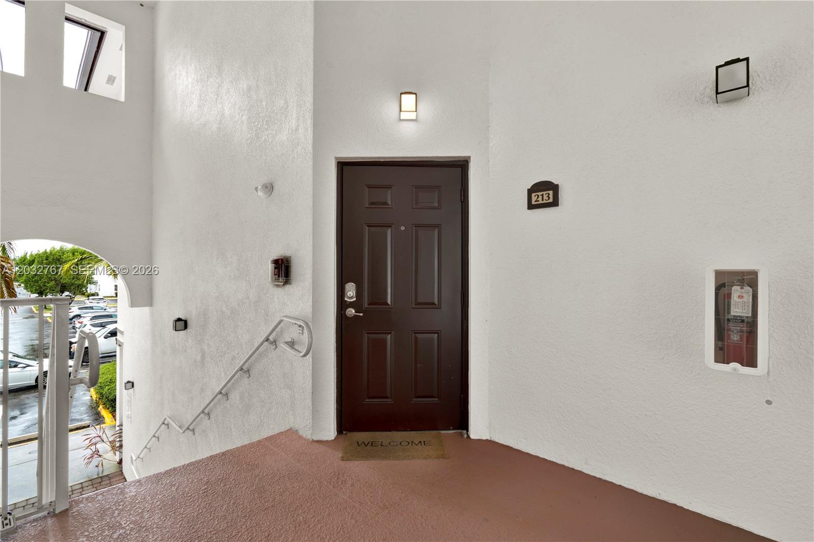 A brown front door with a welcome mat sits at the top of outdoor stairs — 8620 NW 97th Ave # 213, Doral FL 33178, DORAL, FL